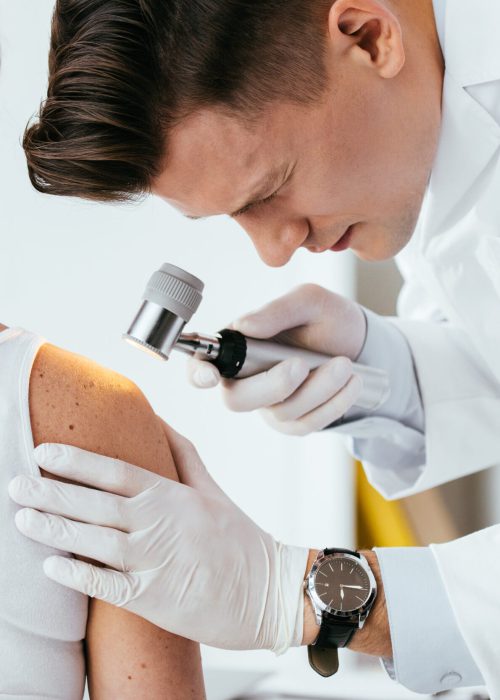 handsome dermatologist holding dermatoscope while examining patient