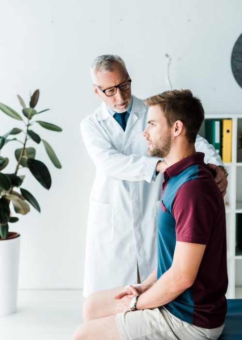 doctor in glasses and white coat touching handsome patient in clinic